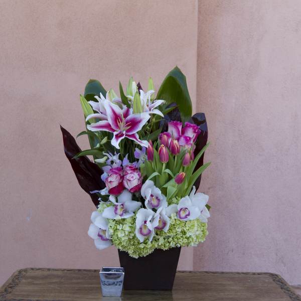 Mixed bouquet of lilies, orchids, and roses in a dark vase