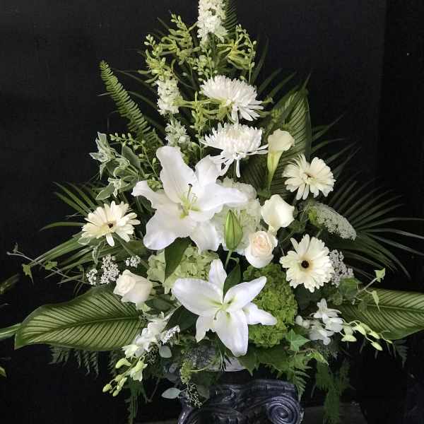 White floral arrangement with lilies, daisies, and roses in a dark vase