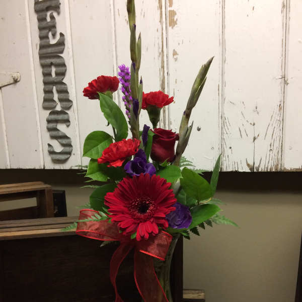 Red and purple flower arrangement in a glass vase with a ribbon