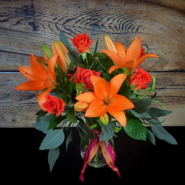 Orange lilies and red roses in a glass vase with a ribbon