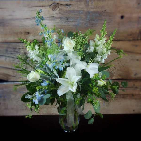 White lilies and roses with blue flowers in a glass vase