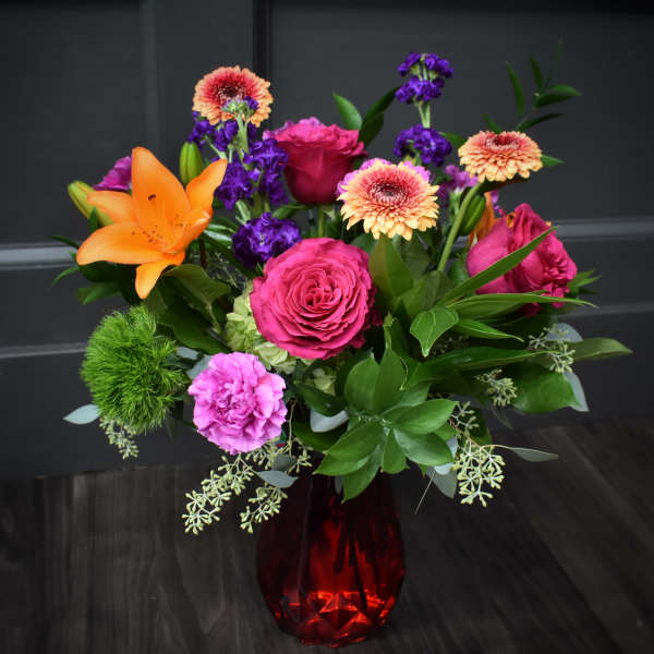 Mixed bouquet of roses, lilies, and gerbera daisies in a red glass vase