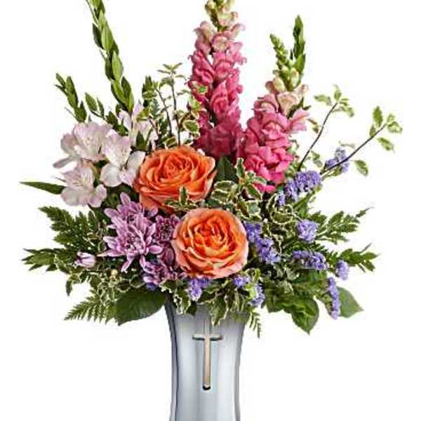 Mixed bouquet of orange roses and pink flowers in a silver vase with a cross