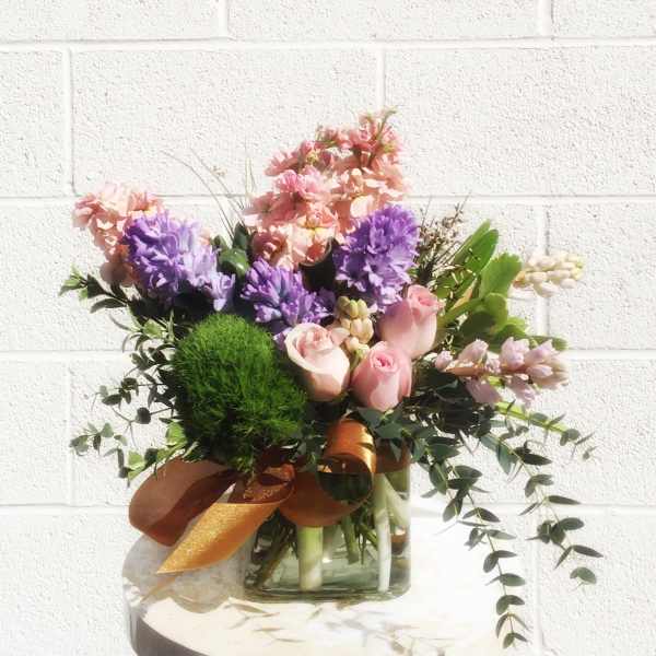 Pink and purple flower arrangement in a glass vase with a ribbon
