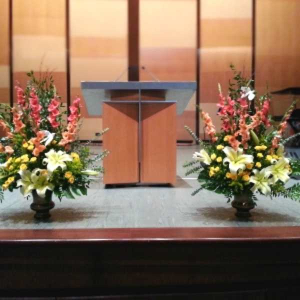 Pair of tall yellow and white lily arrangements with pink blooms on urns flanking a wooden podium