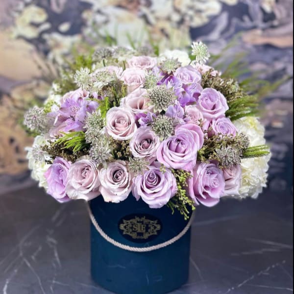 Lavender roses and white filler flowers in a blue hatbox