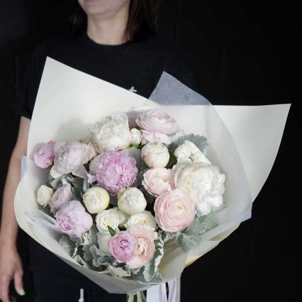 Handheld bouquet of pale pink and white ranunculus wrapped in white paper