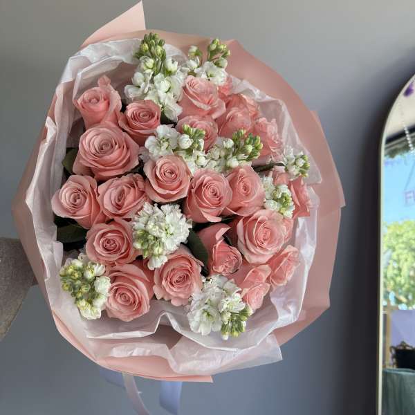 Hand-tied bouquet of pink roses and white stock flowers wrapped in pink paper and tissue