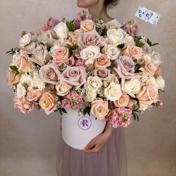 Large hatbox arrangement of cream, blush, and peach roses with pink filler flowers.
