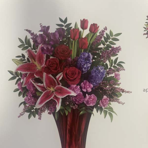 Mixed bouquet of red, pink, and purple flowers in a tall red vase
