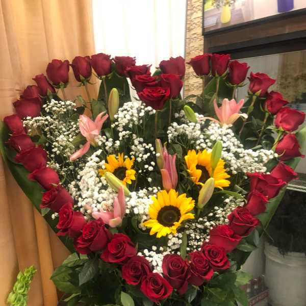 Heart-shaped bouquet of red roses with sunflowers and pink lilies in a white basket
