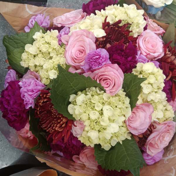 Bouquet of pink roses, hydrangeas, and burgundy flowers wrapped in paper