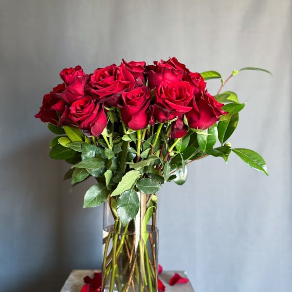 Red roses in a clear glass vase with scattered petals