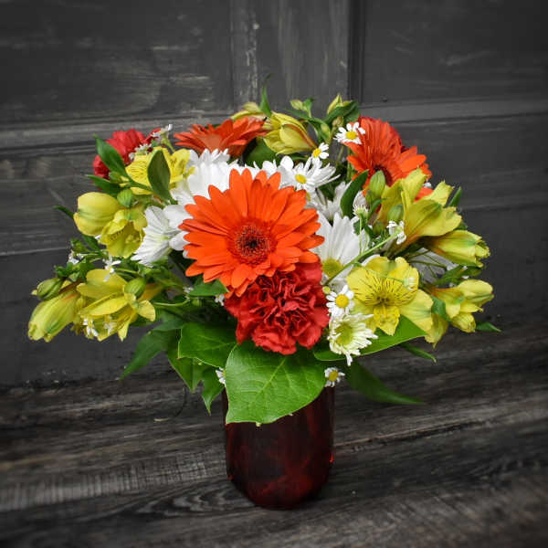 Mixed bouquet of orange, yellow, white, and red flowers in a red vase