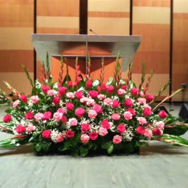 Large pink and white floral stage arrangement with roses and carnations in front of a podium.