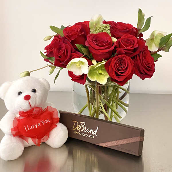 Red roses in a glass vase with a teddy bear and chocolate box