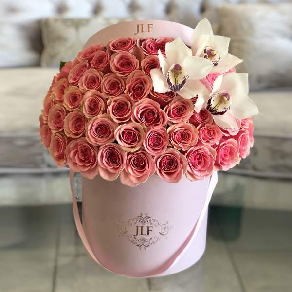 Pink roses and white orchids arranged in a round hat box