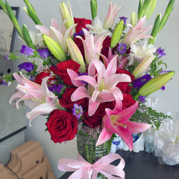 Bouquet of pink lilies and red roses in a glass vase with a pink ribbon