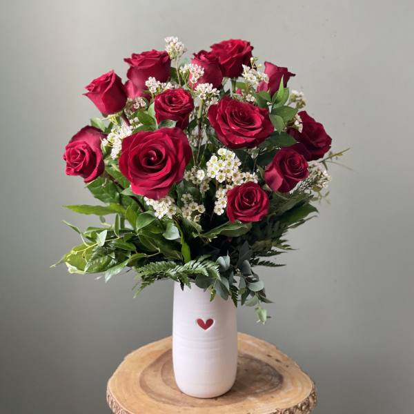 Red roses arranged in a white vase with a small heart accent