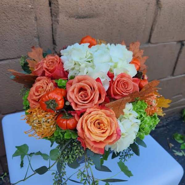 Low arrangement of orange roses, white hydrangeas, mini pumpkins, and trailing vines in a compact mound.