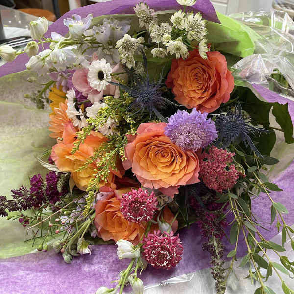 Mixed bouquet with orange roses and purple flowers wrapped in purple paper
