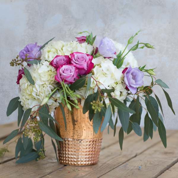 Bouquet of pink roses, white hydrangeas, and lavender blooms in a copper vase