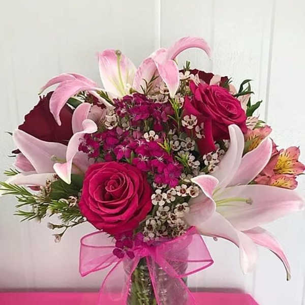 Pink roses and lilies arranged in a glass vase with a pink ribbon
