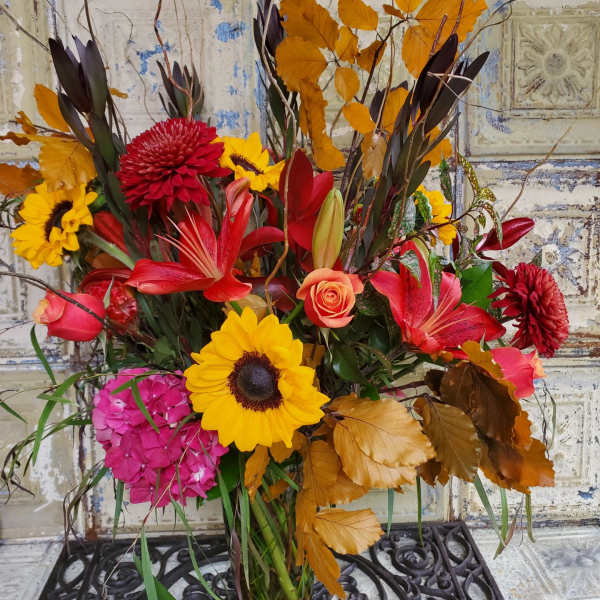 Autumn bouquet with sunflowers, red lilies, and orange leaves in a glass vase