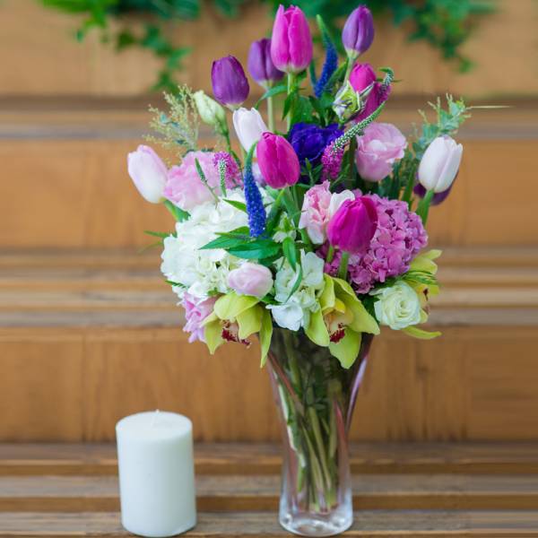 Mixed pink and purple bouquet in a clear glass vase beside a white candle