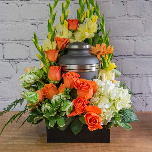 Orange roses and pale yellow flowers arranged around a gray urn