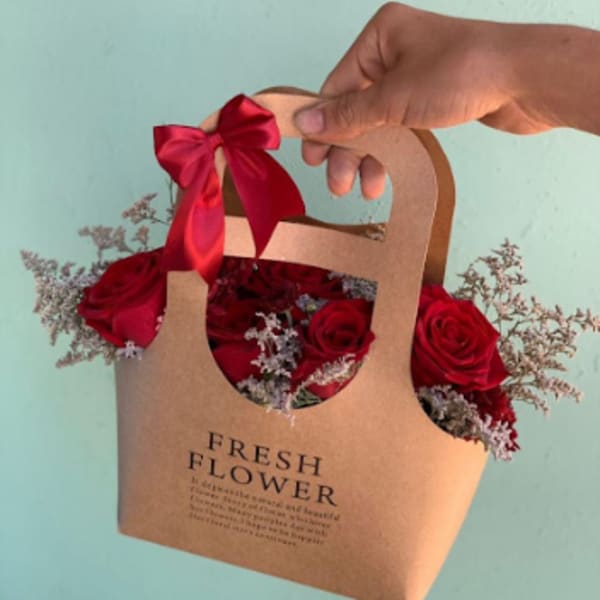 Red roses in a kraft paper gift bag with a red ribbon