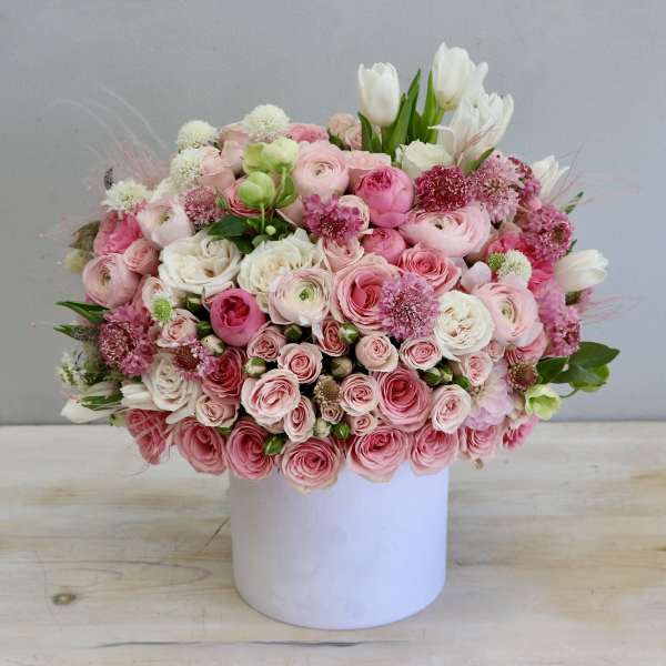 Round arrangement of pink and white roses and ranunculus in a white cylinder container