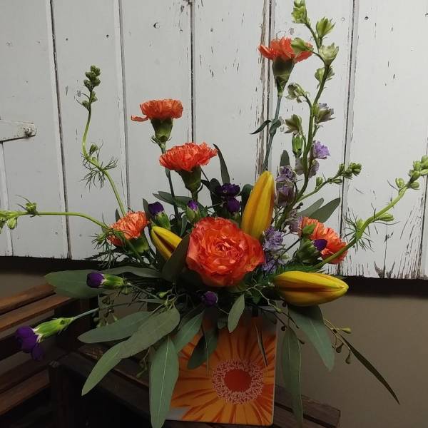 Orange and yellow floral arrangement in a decorative box with tall stems