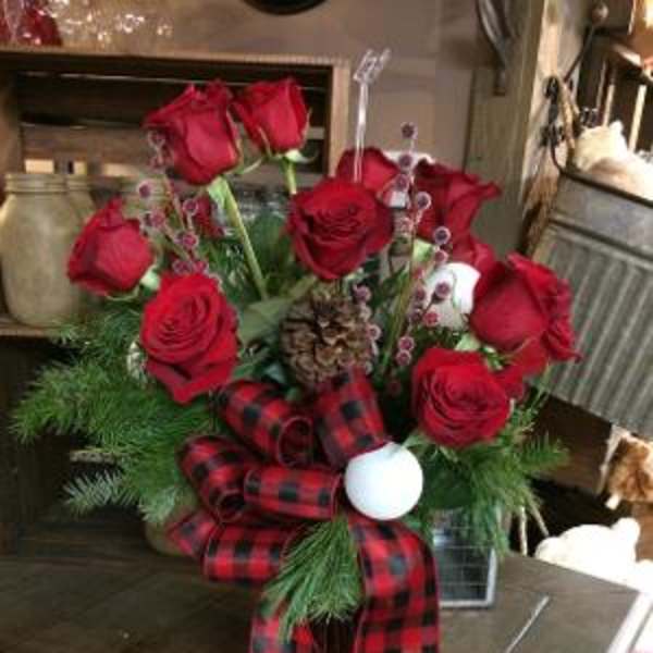 Red roses arranged with plaid ribbon and holiday accents in a vase