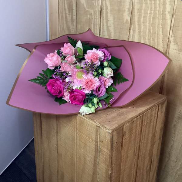 Pink bouquet with roses, carnations, and a daisy-like bloom wrapped in mauve paper