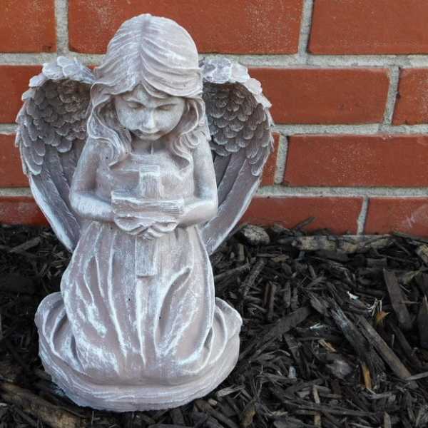 White angel statue holding a candle in front of a brick wall