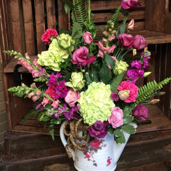 Mixed pink and green floral arrangement in a white ceramic pitcher