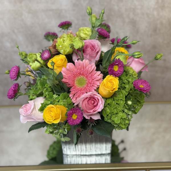 Mixed bouquet with pink and yellow roses, pink gerbera daisy, and green hydrangeas in a vase