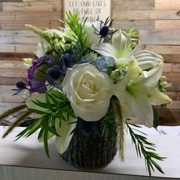 White roses and lilies in a dark textured vase with purple accents