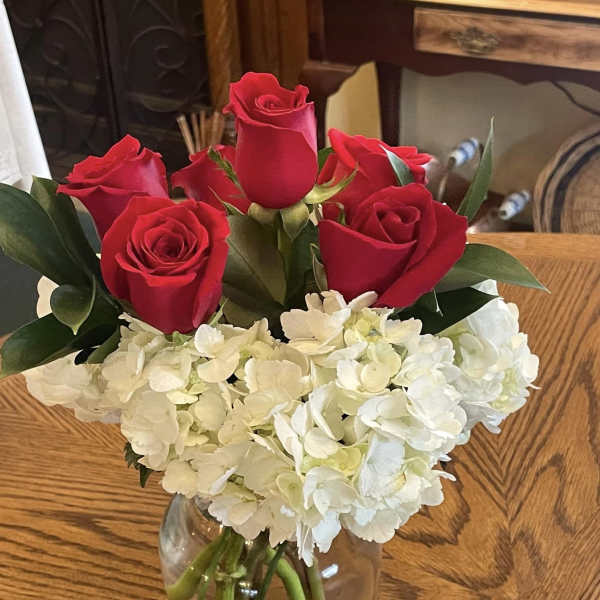 Red roses and white hydrangeas arranged in a clear glass vase