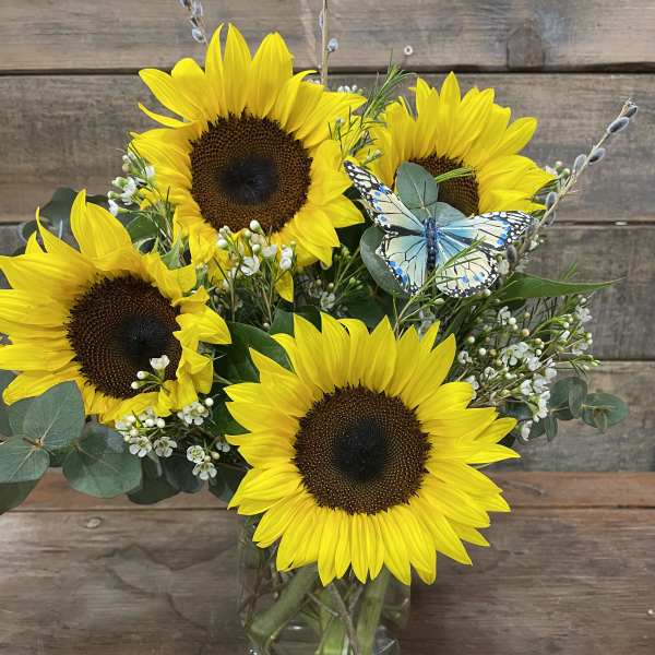 Sunflower bouquet in a glass vase with a butterfly pick