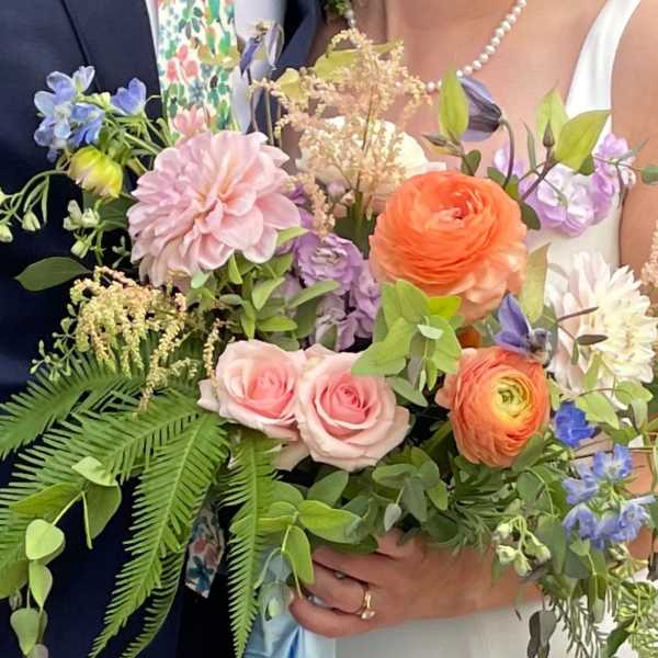 Bride and groom holding pastel wedding bouquets with roses and ranunculus