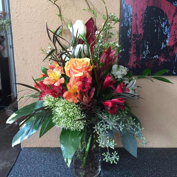 Tall mixed bouquet with orange roses and red lilies in a glass vase