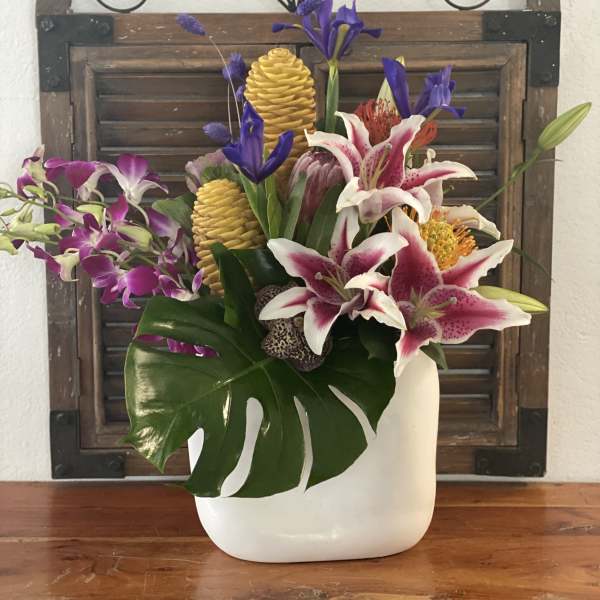 Tropical floral arrangement in a white vase with orchids and lilies