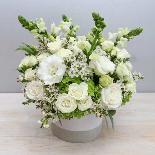 Round white flower arrangement with roses and snapdragons in a white ceramic vase