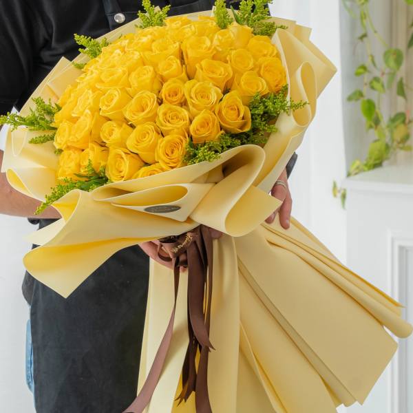 Bouquet of yellow roses wrapped in cream paper with a brown ribbon
