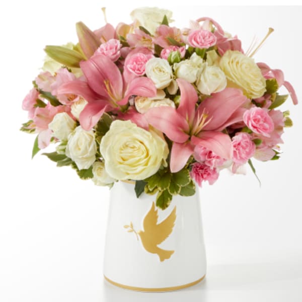 Pink lilies and cream roses arranged in a white vase with a gold dove design.