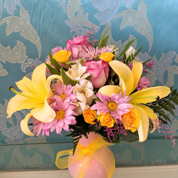 Pink and yellow flower arrangement in a pink vase with a yellow ribbon