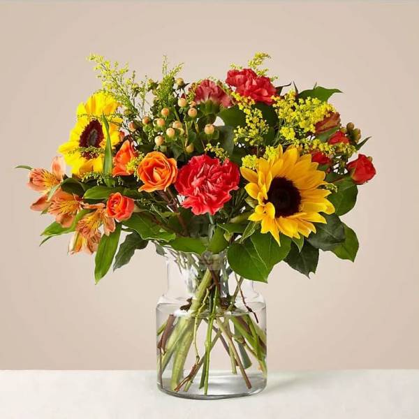 Mixed bouquet of sunflowers, roses, and carnations in a glass vase