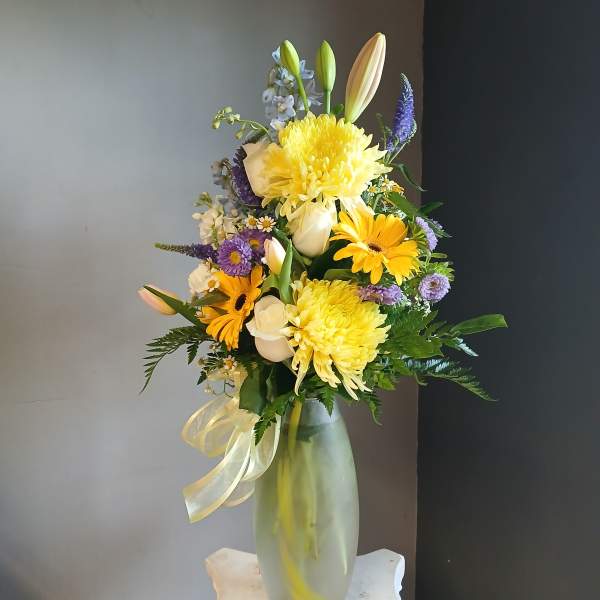 Yellow and white mixed bouquet in a frosted glass vase with a ribbon